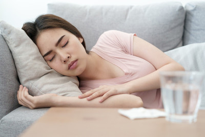 不舒服的状况年轻的亚洲女孩睡在沙发后，检查体温和服用药物和水，健康和疾病概念
