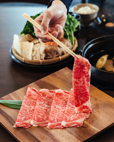 用筷子夹着高大理石纹理的上等和牛A5牛肉，这道菜是素喜烧和日式锅的菜肴。