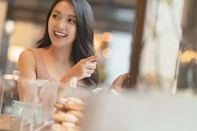 微笑的亚洲女性成年女性幸福愉快地选择精致的巧克力蛋糕和糖果在咖啡馆橱柜展示咖啡馆背景