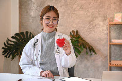 身穿白色制服的女医生，手拿红心，对着镜头微笑。医疗保健和医疗概念。
