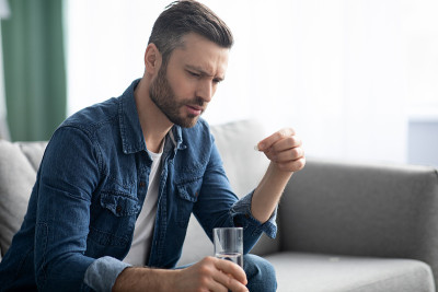 心烦意乱的大胡子男人拿着一杯水在吃药