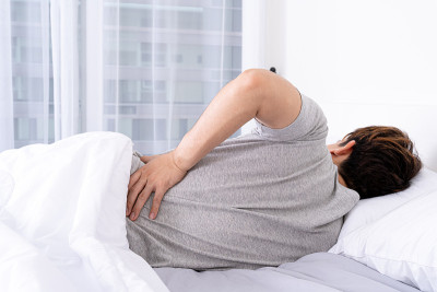 一名年轻人躺在不舒服的床上，背部疼痛。医疗保健或日常生活概念。