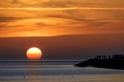 在德国北海的夕阳下，游客们如同剪影般在岸边享受着戏剧性的红色天空，复制空间