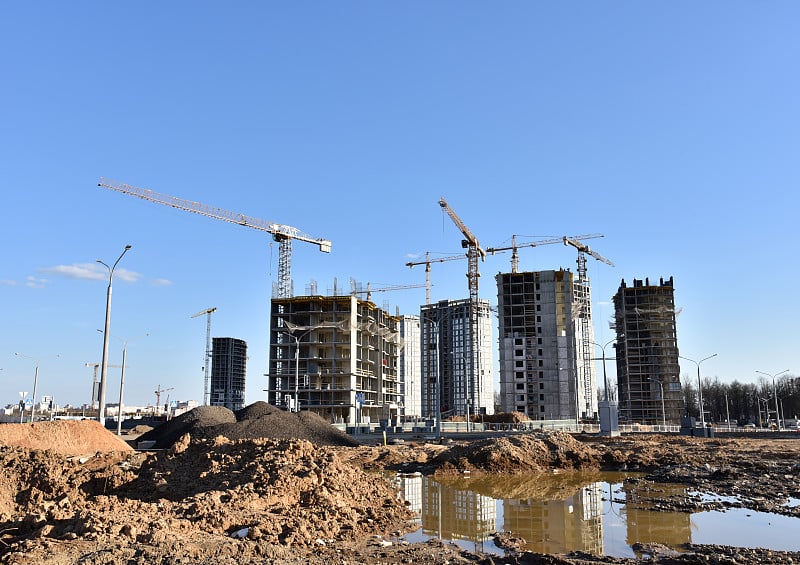 在蓝天下的建筑工地上，塔吊正在建造一座新的住宅楼。建筑行业的改造方案、发展、理念。