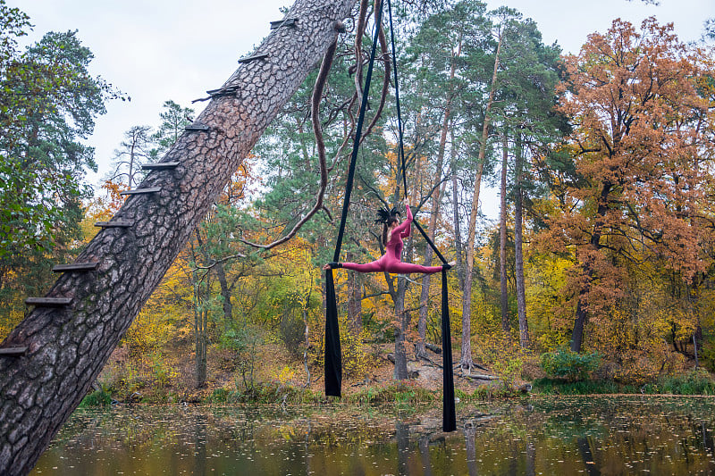 Woman dancing with aerial silk on a trees backgrou