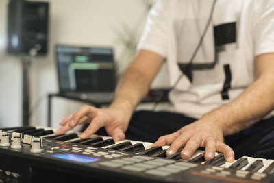 近距离的专业音乐家录制midi键盘在数字工作室在家。他周围都是仪器和迷笛控制器。音乐制作的概念。