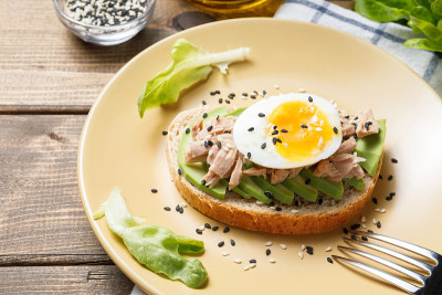 木桌背景上放着鳄梨、金枪鱼罐头和煮鸡蛋吐司。健康食品，早餐或午餐吃鳄梨三明治。