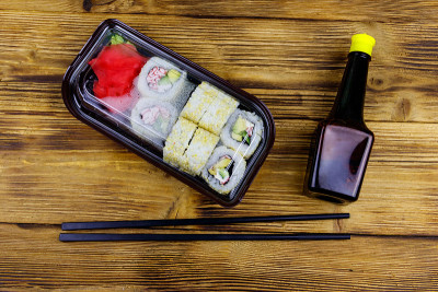 浦崎寿司卷和鱼糜装在塑料盒里放在木桌上。前视图。装在塑料容器内的寿司供外卖或运送