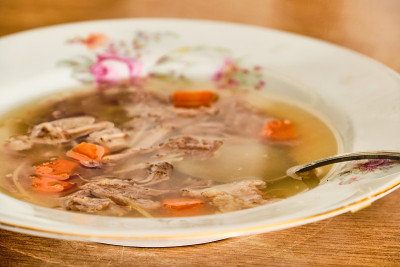 美味的自制牛肉肉汤，胡萝卜面条，白色的盘子和勺子放在木桌上