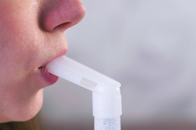 使用喷雾器和吸入器进行治疗。一名年轻女子坐在沙发上，用吸入器的喷嘴对着喉咙吸气。嘴唇和鼻子特写。