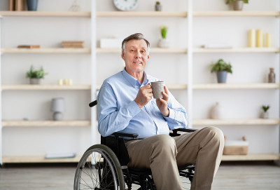 积极的残疾人坐在轮椅上在家喝咖啡或茶