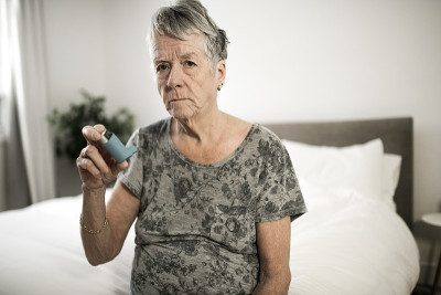 老年妇女在卧室里使用吸入器治疗老年哮喘患者