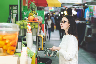 年轻迷人的黑发女人穿着白色毛衣站在附近的街头食品摊位和购买鲜榨果汁在她的午餐时间。她右手拿着一个钱包