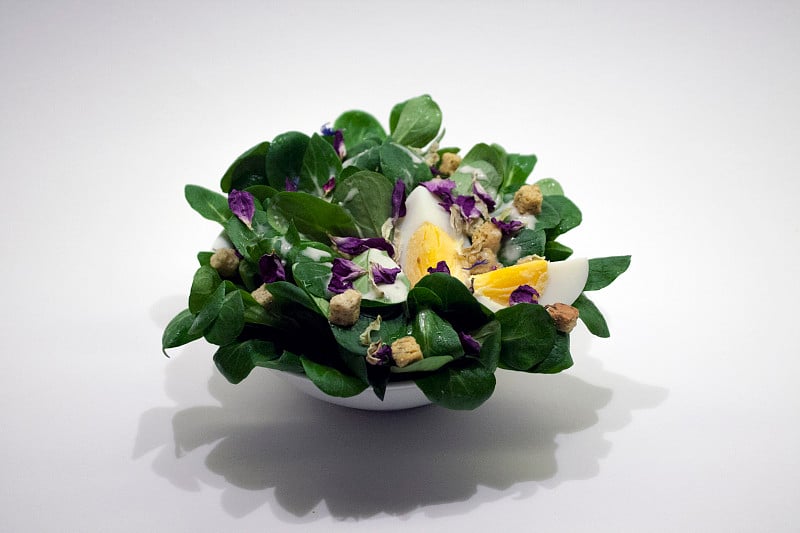 field_salad_with_egg_croutons_and_viola_on_white