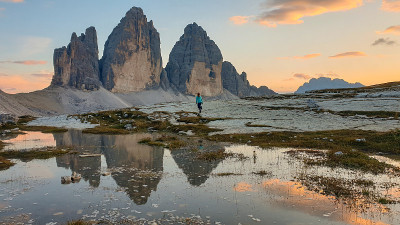 在意大利Dolomites的Drei Zinnen山脉上，一位妇女正在欣赏日落。山峰倒映在船桨上。群