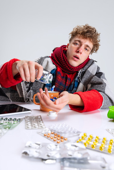 生病的男孩的肖像，患感冒和流感包围的药丸孤立的灰色背景。Self-isolation