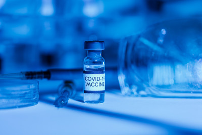 配有试管支架、COVID-19疫苗瓶、注射器、移液管、防护眼镜和培养皿的实验台，蓝光环境