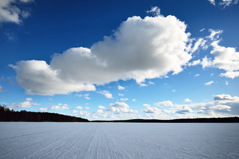 蔚为壮观的蓝天之上是冰雪覆盖的奎托湖，背景是针叶林。冬季景观。乌云。卡累利阿共和国北部拉普兰