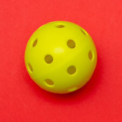 Bright yellow pickleball or whiffle ball on a soli