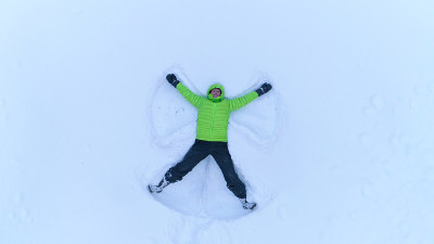 空中的快乐微笑的女孩在雪山的新雪中制作雪角
