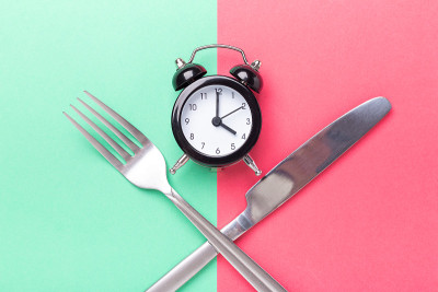 黑色闹钟、叉子、小刀在彩色纸背景上。间歇性禁食的概念