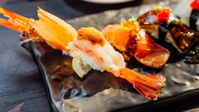 高级寿司套餐包括海胆炸虾、鹅肝、三文鱼、黑石盘、芥末和腌姜。虾寿司的特写。