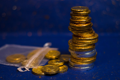许多金币堆在一个角楼和一个装着金币的小袋子里，在蓝色光泽的背景前闪闪发光