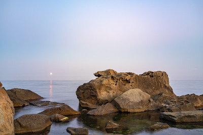 暮色笼罩着荒凉的岩石海滩、海岸线和大海。大海和岩石在夜间的广角视野。