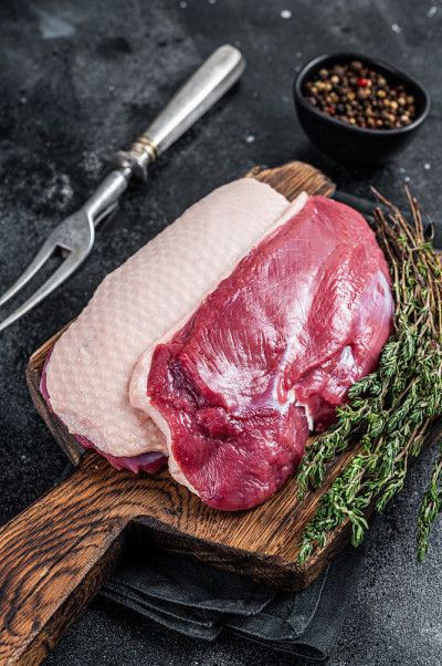 鸭胸肉排，生禽肉放在木板上。黑色背景。俯视图
