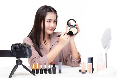 美丽的亚洲女人博客如何化妆和使用化妆品。快乐的亚洲女孩视频博主用相机在社交媒体上分享白色背景的视频。