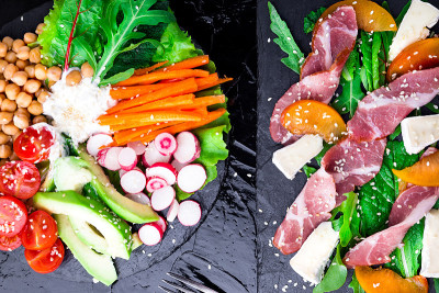 两种不同的沙拉在黑色的石头石板。素食沙拉。肉沙拉。什锦火腿，卡门培尔奶酪，甜瓜，芝麻菜。前视图。