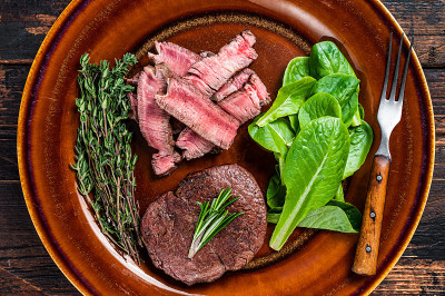 里脊肉、烤里脊肉和切好的牛肉与沙拉放在盘子里。深色木制背景。俯视图