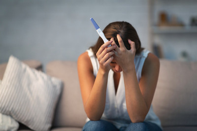 绝望的女人拿着验孕棒坐在家里的沙发上