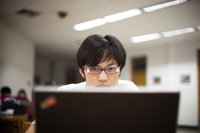 一个戴眼镜的亚洲男学生在用笔记本电脑