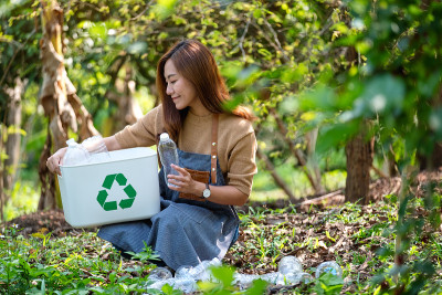 一个美丽的年轻亚洲妇女收集和把塑料瓶放入回收站在户外
