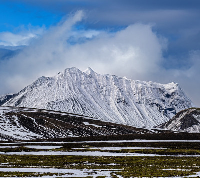 冰岛，秋天冰雪覆盖下多彩的曼那洛加山。前景是火山沙的熔岩场。