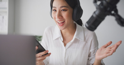 一名年轻的亚洲女性在家庭录音室用笔记本电脑录制播客。