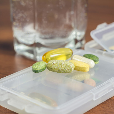 混合天然食品补充剂和维生素丸的塑料容器在木桌。