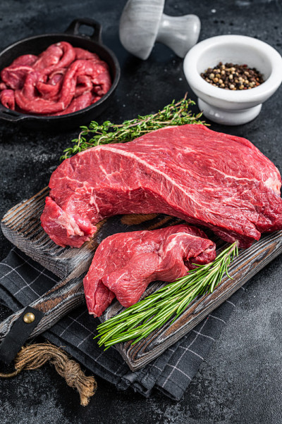 圆形切好的牛肉片放在砧板上。黑色背景。俯视图