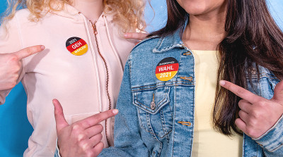 两个年轻的女人用手指着衣服上的选举按钮。声明:“2021 Geh Wählen”(2021 Go V