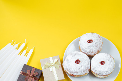 光明节快乐。黄色背景的犹太甜点Sufganiyot。犹太教节日的象征。甜甜圈、蜡烛和礼物。