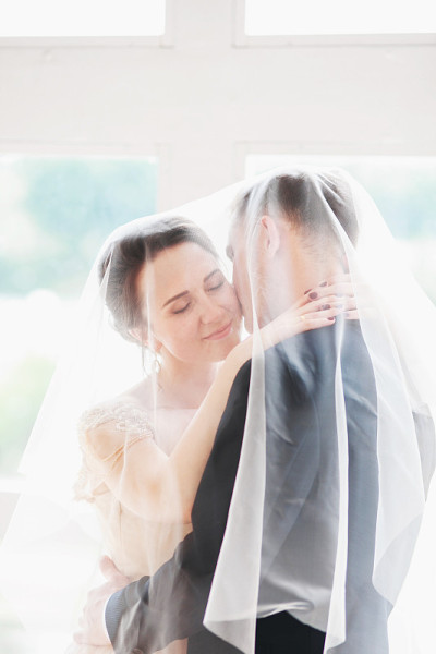 美丽的新娘和新郎肖像与面纱的脸。时尚恩爱的新婚夫妇亲吻和拥抱