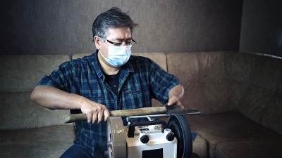 蒙面亚洲人在磨床上磨斧头。工作过程