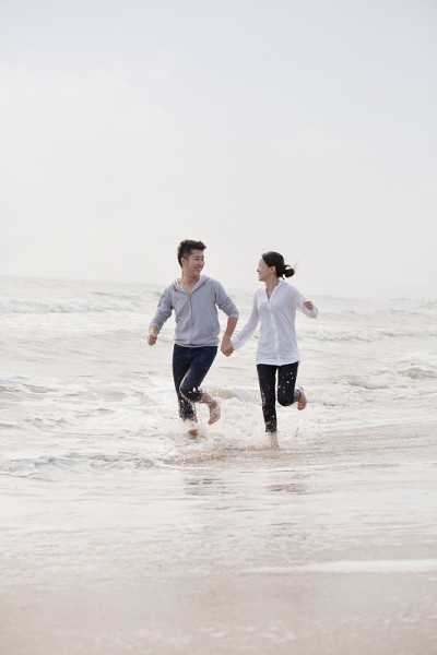 中国，一对年轻夫妇手牵着手在海滩边跑步
