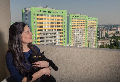 一个带着黑猫的女孩从阳台看向一座新楼