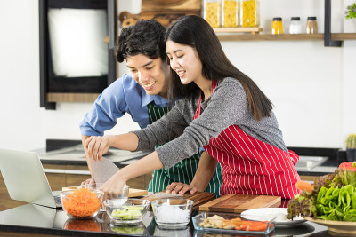 穿着围裙的亚洲夫妇在厨房里用笔记本。