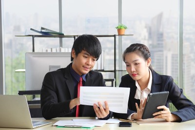 在以现代都市景观为背景的正式商务办公室里，穿着正装的亚洲商务人士正在讨论年度报告