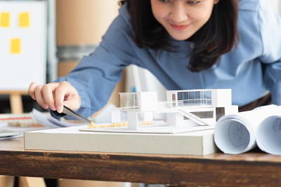 在建筑工作室中，建筑师女性用镊子在现代家庭模型上制作一个模拟灌木，建筑设计师或建筑师学生概念