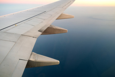 从飞机上看飞机白色的机翼在阳光明媚的早晨飞过海洋景观。航空旅行和运输概念。