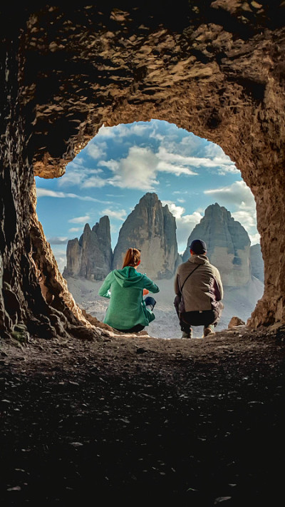 一对夫妇坐在一个山洞前，欣赏着意大利Dolomites的Drei Zinnen。他们正在欣赏宁静的风